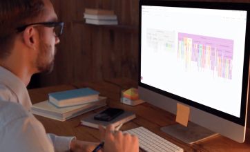 A man in glasses sits at a desk looking at a graph on his computer screen