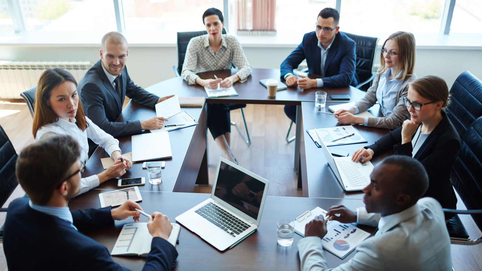 Group of diverse professionals in a conference room discussing strategies related to drunk driving organizations, with laptops, documents, and notepads on the table.