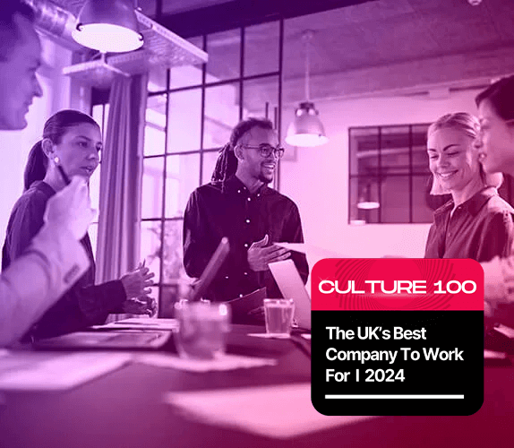 Group of professionals engaging in a lively discussion in a modern office space. By clicking on this image, you will be directed to a third-party article titled 'Introducing the Culture 100 Awards for 2024,' which highlights the top UK companies to work for in 2024.